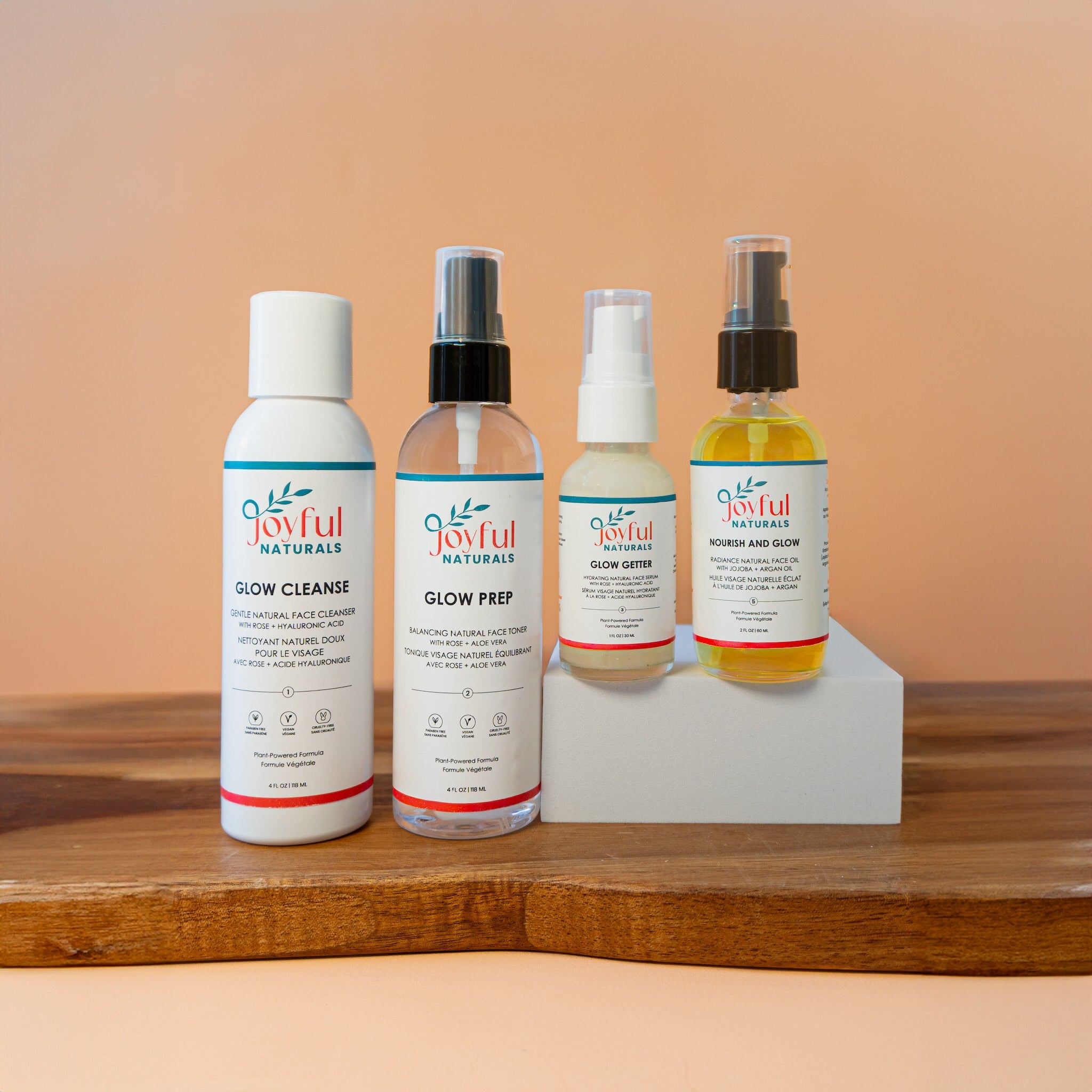 Joyful Naturals Glow System 4-step skincare routine set with cleanser, toner, serum, and jojoba oil on peach background.